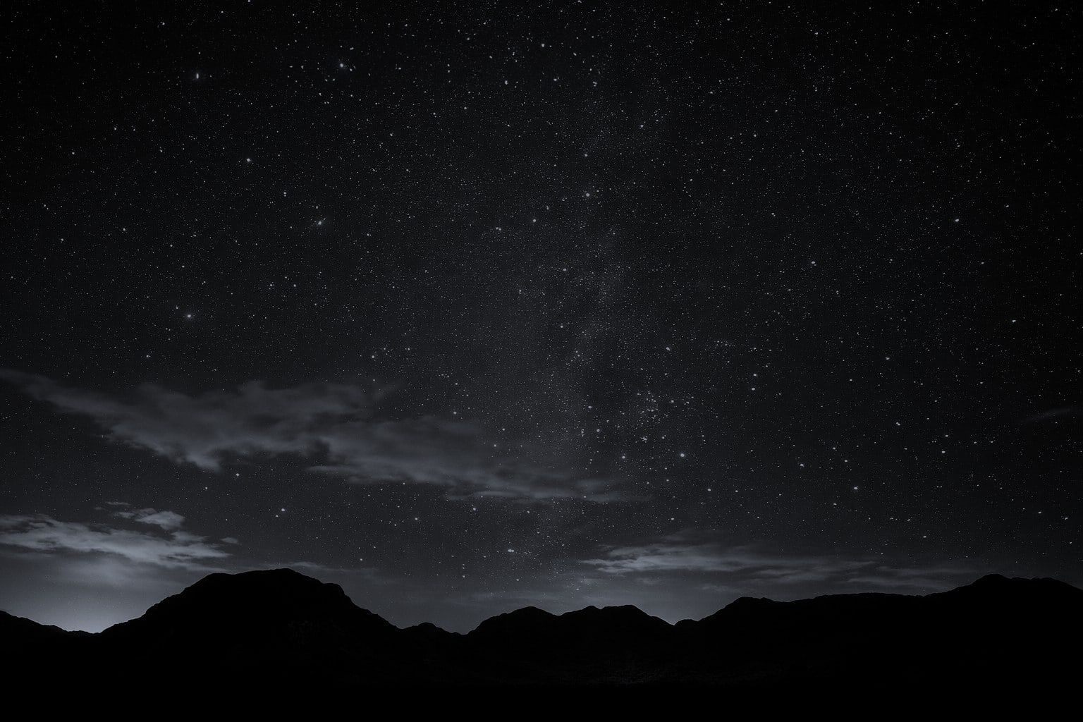 A night sky full of stars over a dark mountain ridge.